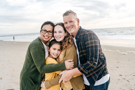 A family of 4 standing at the beachfront. The wife is putting on eyeglasses.