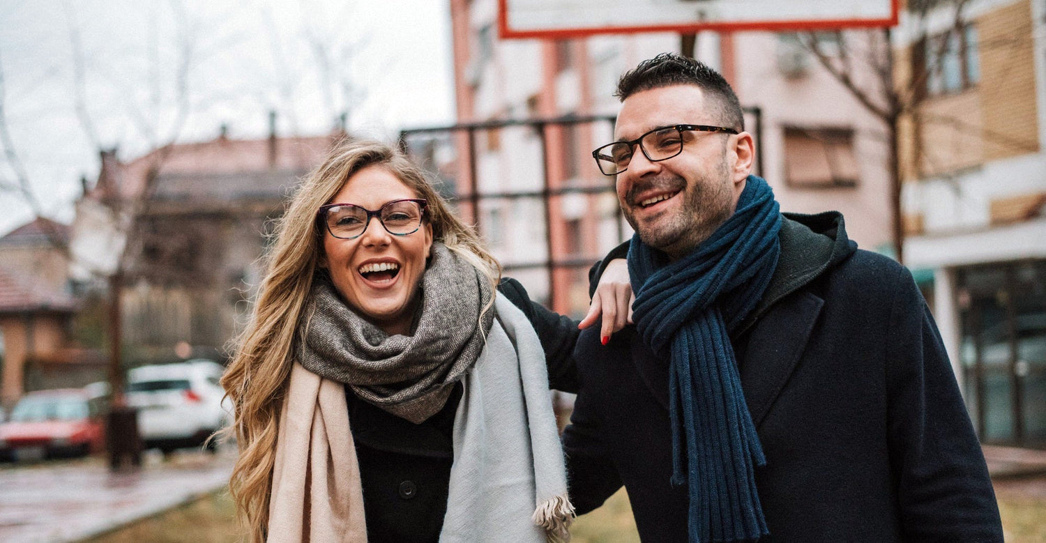 A couple is walking on the street and smiling. They are both wearing eyeglasses with great lenses